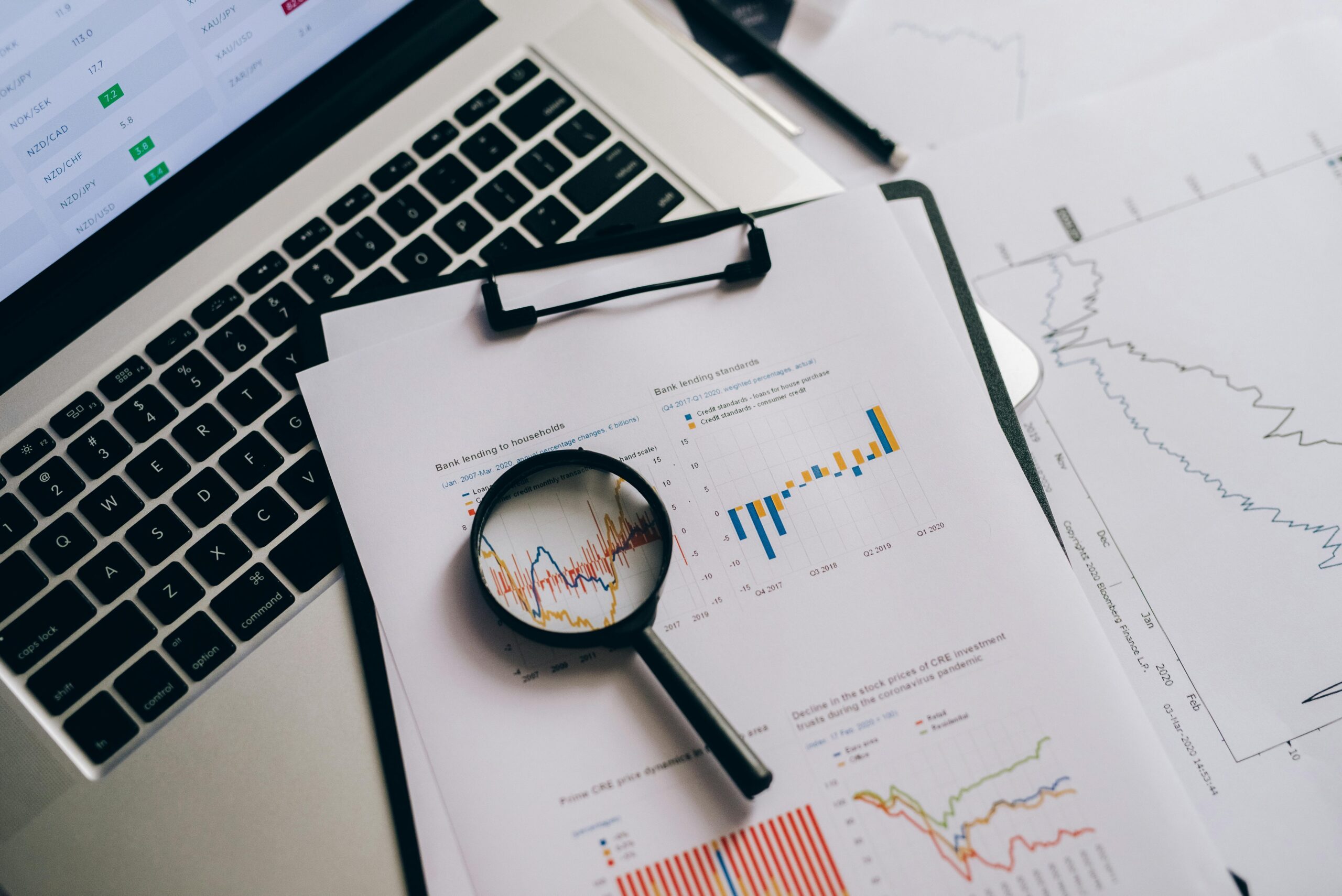 Laptop with financial data on screen, magnifying glass over printed graphs and charts, analyzing tax audit trends and statistics.